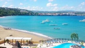 Un resort con piscina, playa y barcos al fondo.