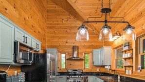 A modern kitchen with wooden walls, stainless steel appliances, and a central island with bar stools. - Luxury Cabin centrally located to all the things to see and do in High Country! (Banner Elk)