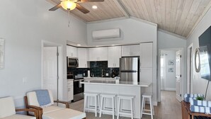 A modern kitchen with white cabinets, a stainless steel refrigerator, and a built-in oven. There is a dining area with a wooden table and white chairs. - Golf Cart Included, Cat Island Villa, Treasure Cay, Bahamas (Treasure Cay)