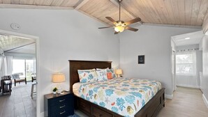 A bedroom with a wooden ceiling fan, a bed with a floral bedspread, a nightstand with a lamp, and a view of an outdoor patio. - Golf Cart Included, Cat Island Villa, Treasure Cay, Bahamas (Treasure Cay)
