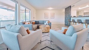 Een moderne woonkamer met een hoekbank, twee fauteuils, een salontafel en een keukenhoek met barstoelen.
