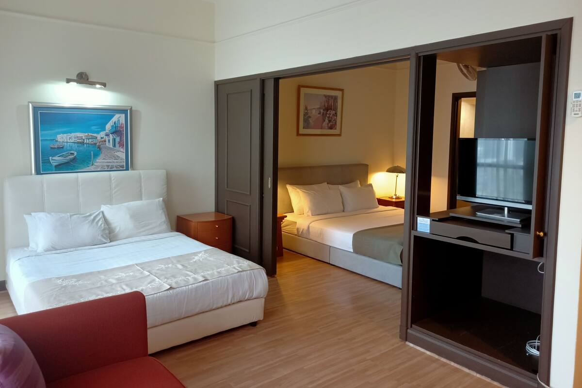 Ein Hotelzimmer mit einem großen Bett, einem kleineren Bett, einem Fernseher und einem Bild an der Wand.