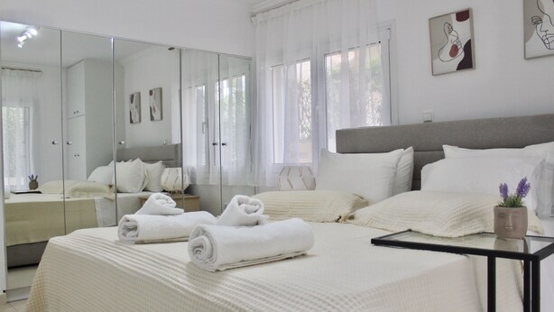 A modern bedroom with a large bed, a bedside table, a mirror, and a view of the outdoors.