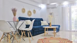 A modern living room with a blue sofa, white chairs, a glass dining table, and a colorful woven rug.
