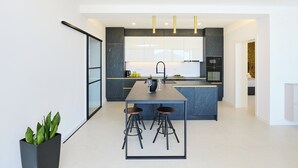 A modern kitchen with a central island, bar stools, and a potted plant. - Hedera Estate, Hedera A25 (Lozica)