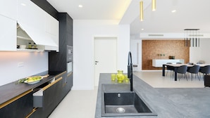 A modern kitchen with a built-in oven, a sink, and a dining area with a table and chairs. - Hedera Estate, Hedera A25 (Lozica)