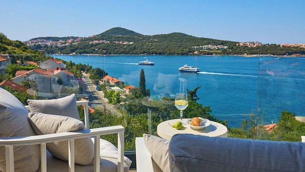 A balcony with a glass barrier overlooking a coastal town, a glass of wine, and a plate with food. - Hedera Estate, Hedera A25 (Lozica)