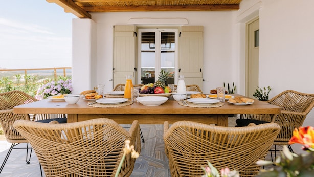 Un coin repas avec une table en bois dressée pour quatre personnes, entourée de chaises en osier, et offrant une vue sur l’extérieur.