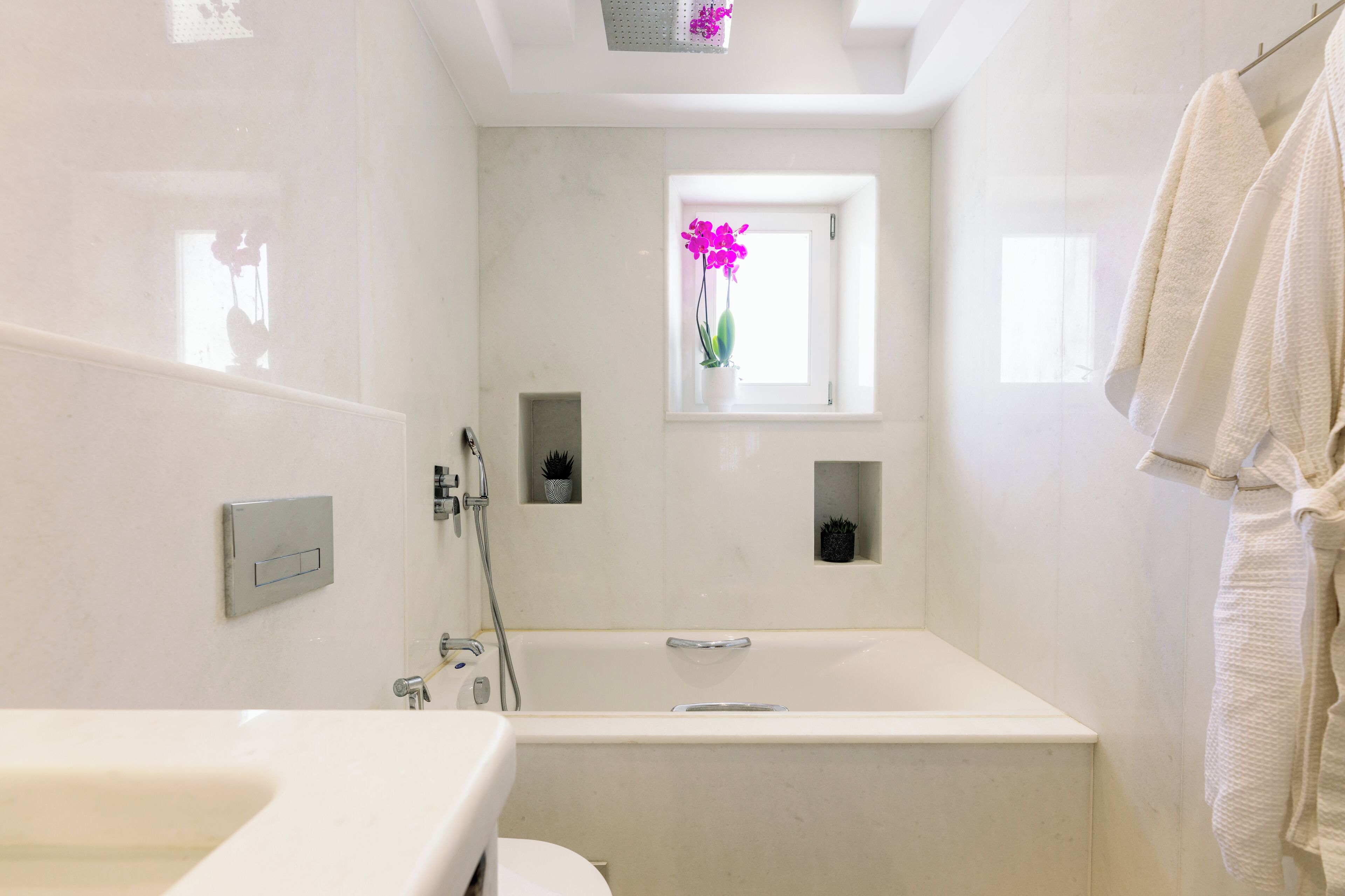 A modern bathroom with a bathtub, a sink, and a window with a potted orchid.
