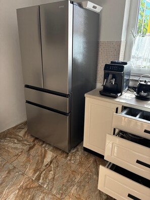 Una cocina con un refrigerador de acero inoxidable, una cafetera y un armario blanco con cajones.
