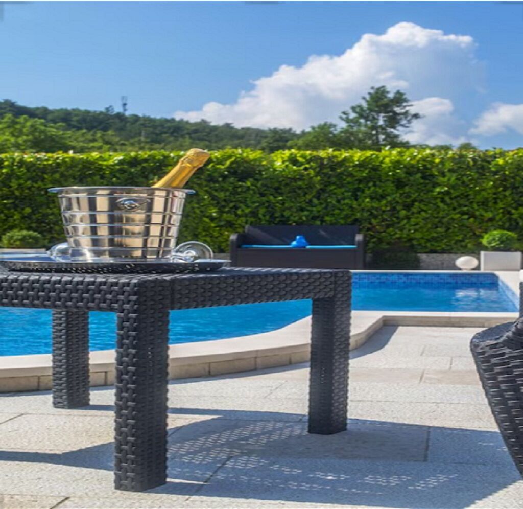 Un espace aménagé au bord de la piscine, avec une table en osier, un seau en métal et un barbecue.