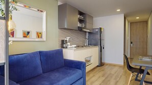 A compact living space with a blue sofa, a kitchenette with a coffee maker, and a refrigerator. - gA Distintivo Loft en Cabrera (Bogotá)