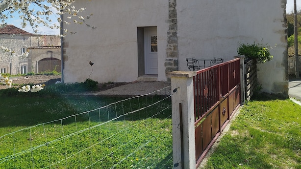 Un bâtiment blanc avec un toit rouge, une petite porte et un jardin clos.