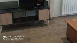 Un salon avec un téléviseur à écran plat posé sur un meuble en bois, un petit placard et un radiateur blanc.