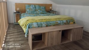 Une chambre à coucher avec une tête de lit en bois, un lit recouvert d’une couvre-lit à motifs floraux, deux tables de chevet avec des lampes et un banc en bois au pied du lit.