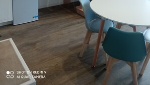 Un espace de vie compact comprenant un escalier en bois, un petit réfrigérateur, un four à micro-ondes et une table ronde avec des chaises.