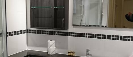 Een moderne badkamer met een wit toilet, een wastafel en een spiegel. Er zijn zwarte kastjes en een douchecabine met glazen wanden.