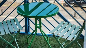 Een balkon met een groene metalen tafel en twee groene metalen stoelen, met uitzicht op een jachthaven met boten en gebouwen op de achtergrond.