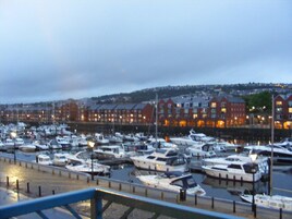 A marina with numerous boats docked, a waterfront promenade, and residential buildings in the background.