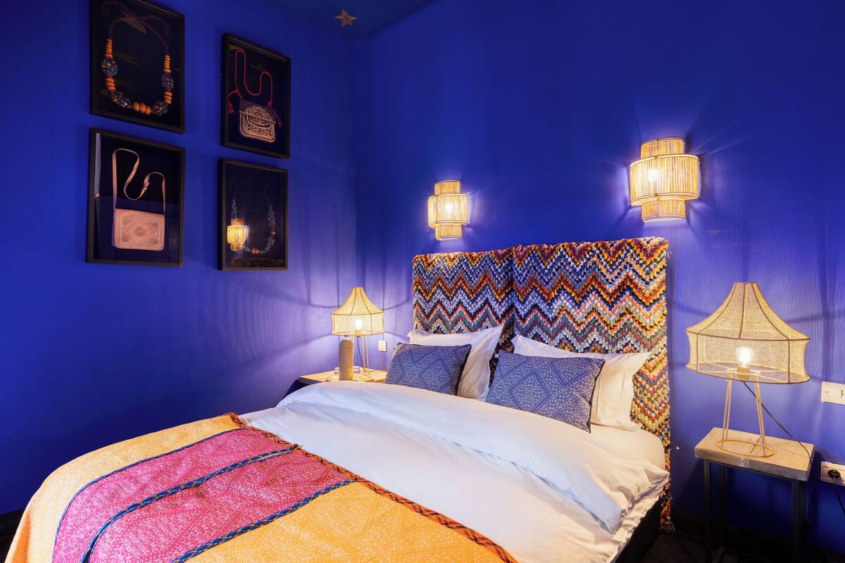 A bedroom with a blue wall, a bed with a colorful headboard, and framed items on the wall.