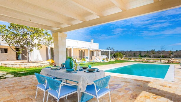 An outdoor patio with a table set for dining, a swimming pool, and a white building in the background. - Villa Angelita by Villa Plus (Ceglie Messapica)