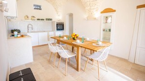 A compact kitchen with white cabinets, a wooden dining table, and white chairs. - Villa Angelita by Villa Plus (Ceglie Messapica)