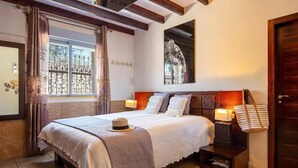 Een goed verlichte slaapkamer met een groot bed, een nachtkastje met een lamp en een deur.