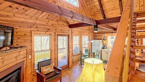 A wooden cabin interior with a fireplace, a dining area, and a large window. - Peaceful Waters Ridge on the Soque River (Demorest)