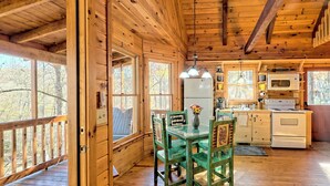 A wooden cabin interior with a dining area, kitchen, and large windows. - Peaceful Waters Ridge on the Soque River (Demorest)