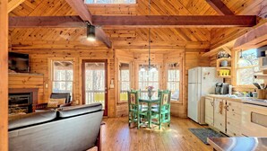 A cozy cabin interior with a wooden interior, a dining area with a table and chairs, a kitchen with a refrigerator and cabinets, and a fireplace. - Peaceful Waters Ridge on the Soque River (Demorest)