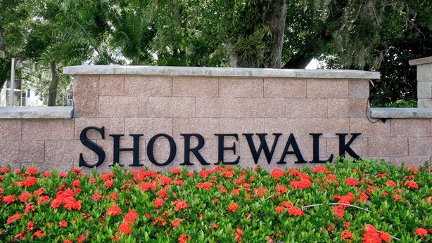 A stone wall with the word "Shorewalk" in large letters, surrounded by a garden with red flowers.