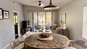 A modern living room with a round wooden table, a ceiling fan, and a television.