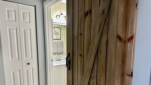 A white door with a handle, a wooden door with a handle, and a bathroom with a sink and mirror.