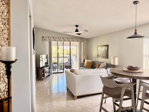 A spacious living room with a large sofa, a dining table with chairs, a ceiling fan, and a TV.