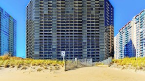 Een hoog gebouw met een raster van ramen, een zandkleurige voorgrond en een helderblauwe lucht.