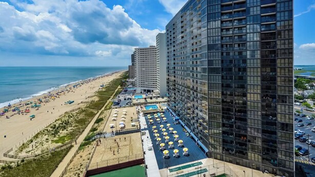 Een hoog hotel met meerdere balkons, uitzicht op het strand en een zwembad.