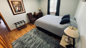 Een slaapkamer met een bed, een stoel, een bureau, een lamp en een lijst aan de muur.