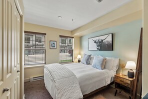 A bedroom with a large bed, two bedside lamps, a framed picture on the wall, and a window with blinds. - First Tracks Studio w/ Pool, Gym, Gondola Access (Steamboat Springs)