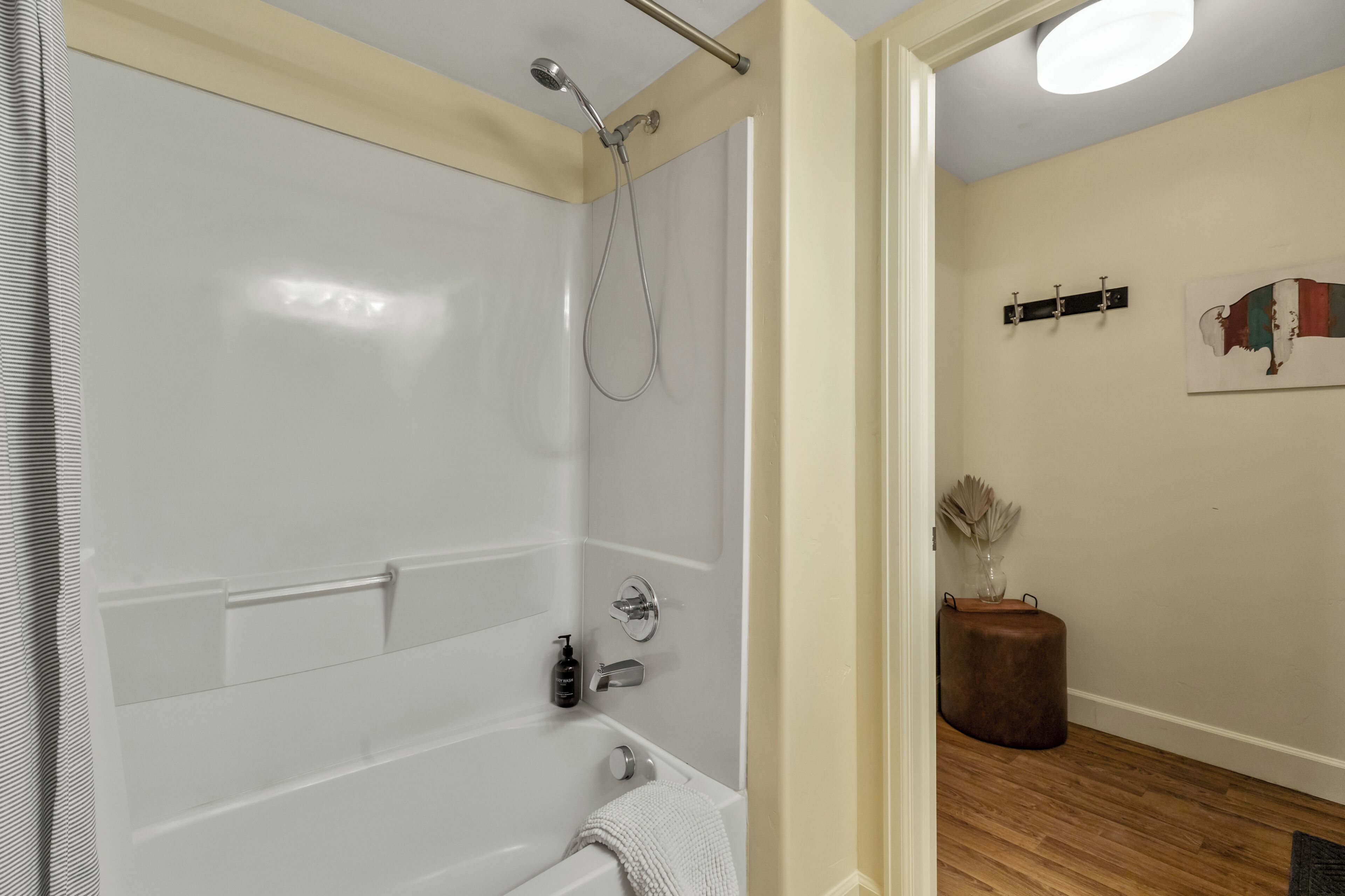 A modern bathroom with a shower, a bathtub, and a toilet. There is a towel hanging on the wall, a small stool, and a wall-mounted towel rack.