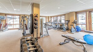 Un gimnasio con diverso equipo de ejercicio, amplias ventanas y piso alfombrado.