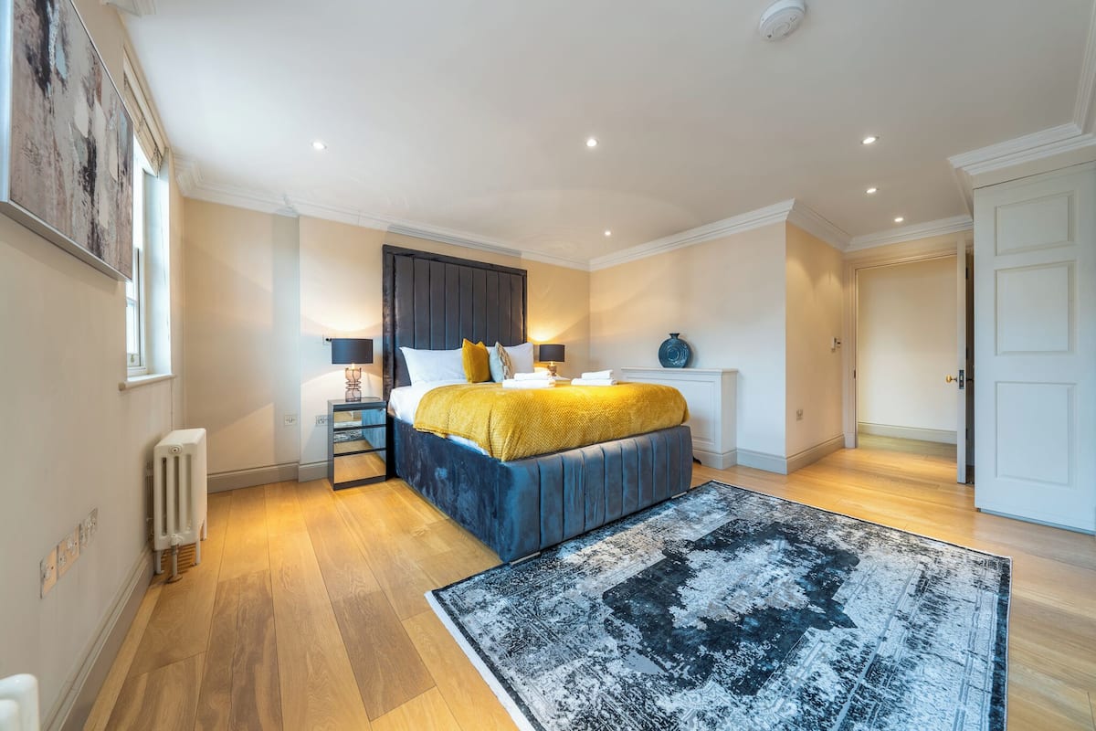 Ein Schlafzimmer mit Bett, Nachttisch, Lampe, Heizkörper und einem großen Teppich.