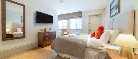 A bedroom with a bed, a dresser, a TV, and a large mirror.