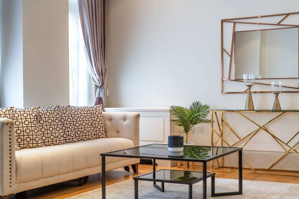 Ein Wohnzimmer mit einer Couch, einem Glastisch, einem Konsolentisch mit goldener Rahmung und einem großen Spiegel.
