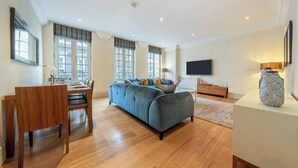 A modern living room with a sofa, dining table, and TV. - The Mayfair Collection (London)
