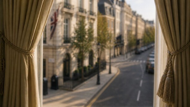 A view through curtains of a street with buildings, a flag, and a tree. - The Mayfair Collection (London)