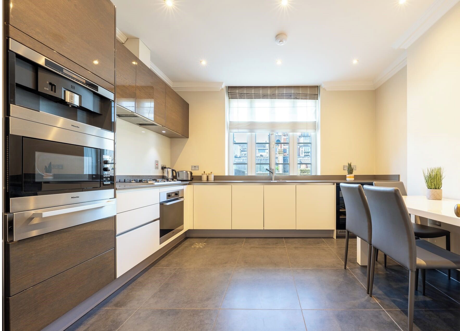 A modern kitchen with stainless steel appliances, a large window, and a dining area with a table and chairs.