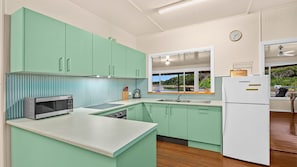 Une cuisine avec des armoires de couleur turquoise, un réfrigérateur blanc et une fenêtre donnant sur un paysage naturel.