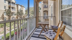 A balcony with a table and chairs, a view of neighboring buildings, and a clear sky. - Disney 2 miles w/Heated Pool, water park, basketball tennis courts,  game room  (Kissimmee)
