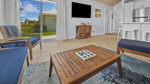 Een ruime woonkamer met een houten salontafel, een aan de muur bevestigde televisie en een balkon met uitzicht op groen en een heldere lucht.