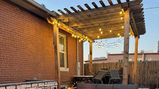A patio with a stone fire pit, outdoor furniture, and a pergola with string lights. - Cozy, custom bungalow in the heart of the Sante Fe Art District! (Denver)